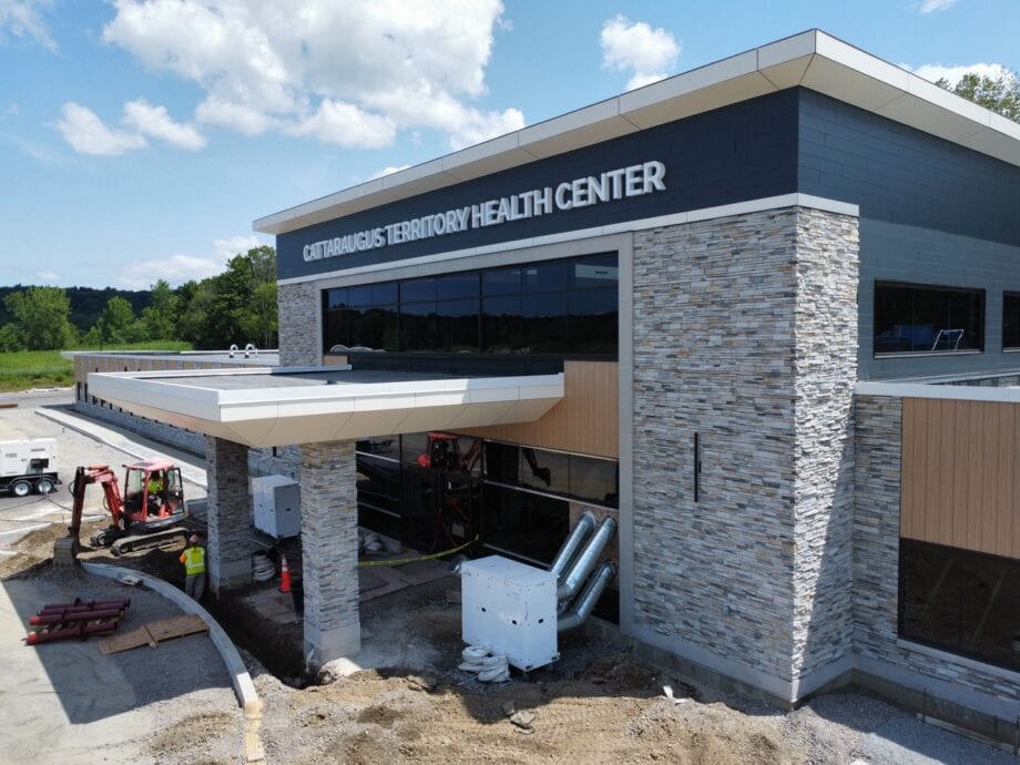 A front image of construction of the Cattaraugus Health Center – Seneca Nation of Indians, featuring a combination of Max Compact Exterior phenolic panels in Carbon Grey, a sleek, solid dark decor, and Enigma Oak, a light, textured woodgrain